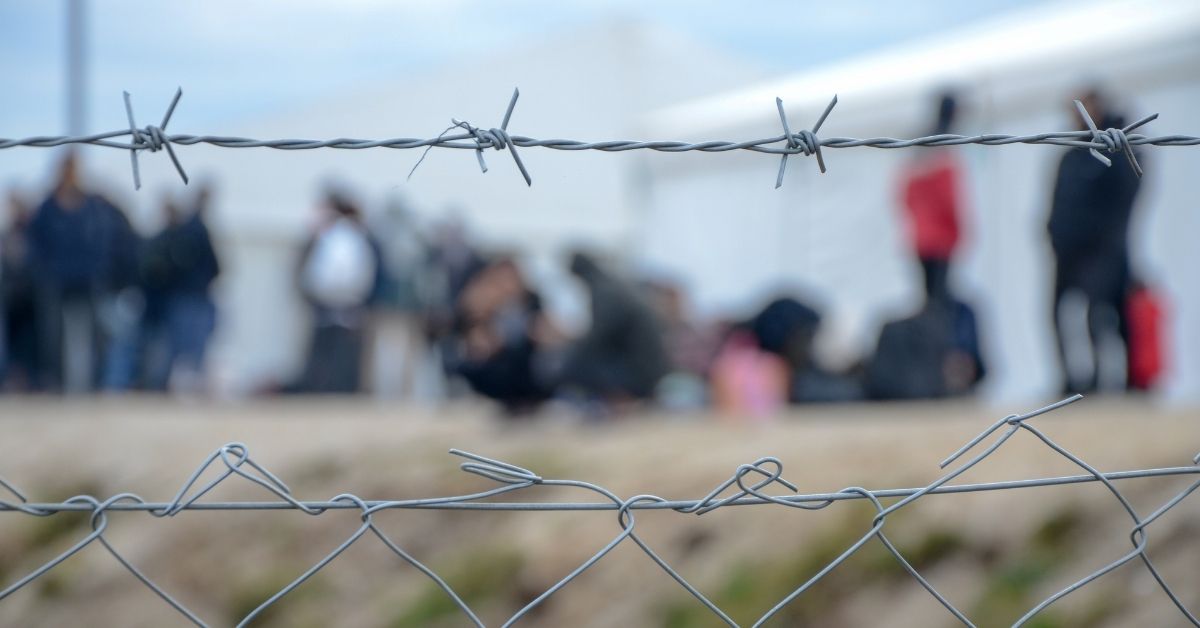 Line of people off focus seen through bar-wired fence